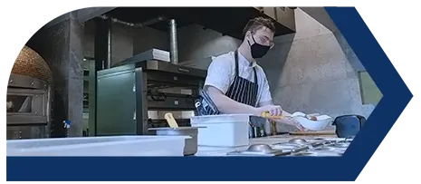 Hombre trabajando en una cocina de panadería, con un mesa con instrumentos de cocina y un horno al fondo